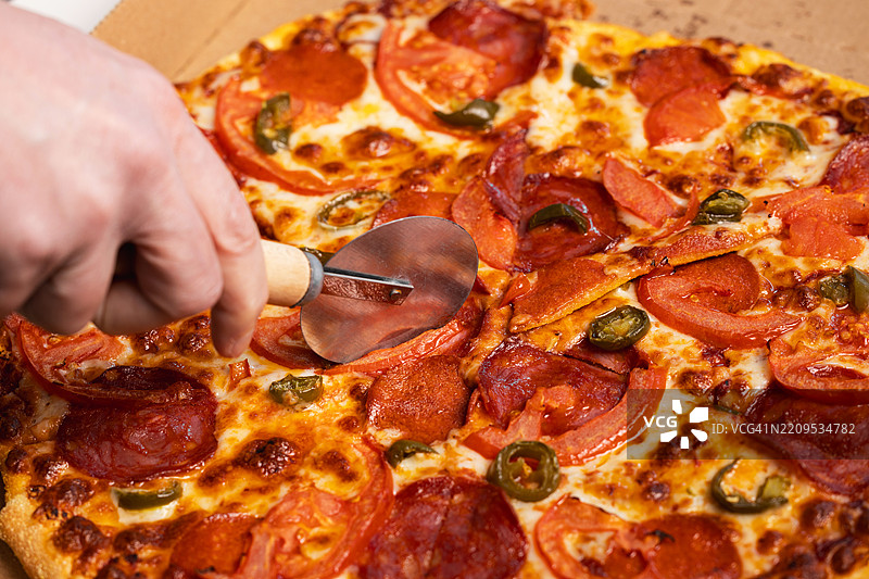 手用披萨刀切割意大利香肠和西班牙香肠披萨图片素材
