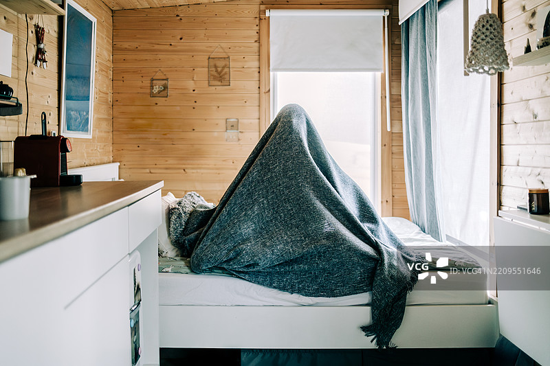 坐在床上躲在毯子下的人图片素材