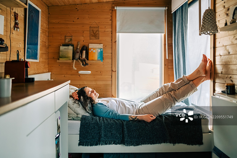 女人在她的小房子卧室里放松，双脚靠在墙上。图片素材