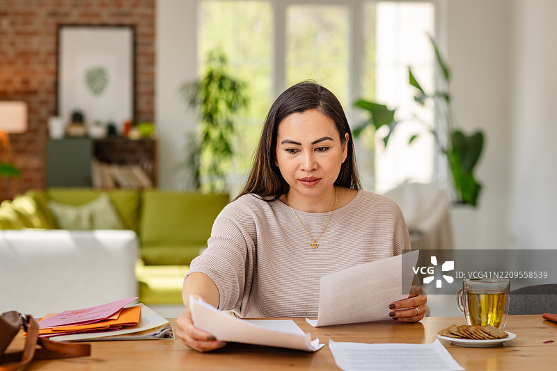 老师在舒适的客厅环境中享受她的晚上，边审阅工作边放松，手里拿着一杯茶和小吃。图片素材