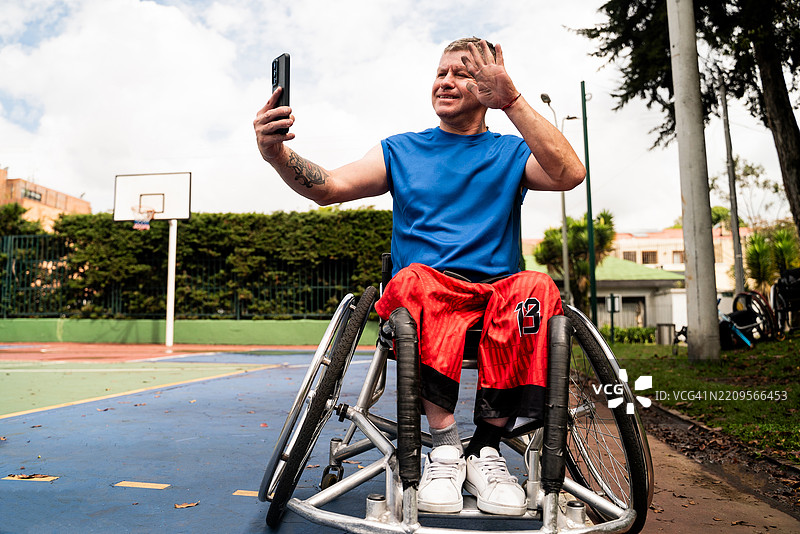 成熟的运动员男子在运动场上用轮椅进行视频通话图片素材