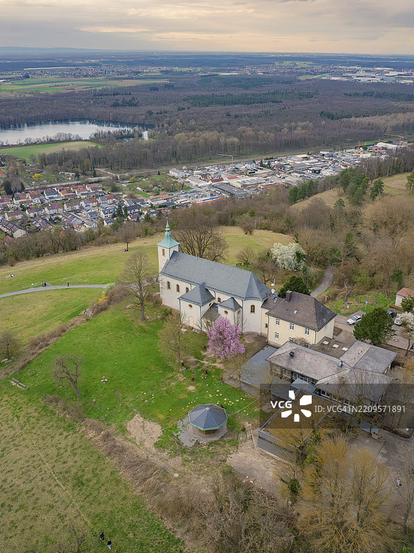 教堂与周围建筑坐落在山丘上，四周被树木环绕，呈现出如画的春季全景，米歇尔斯贝格，巴德明斯特赖费尔图片素材