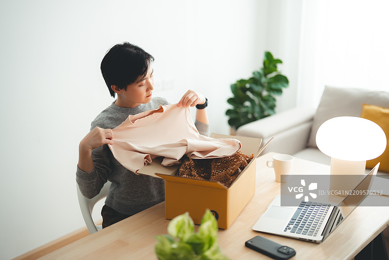 亚洲女性在家办公时开心地享受网上购物的开箱体验。图片素材