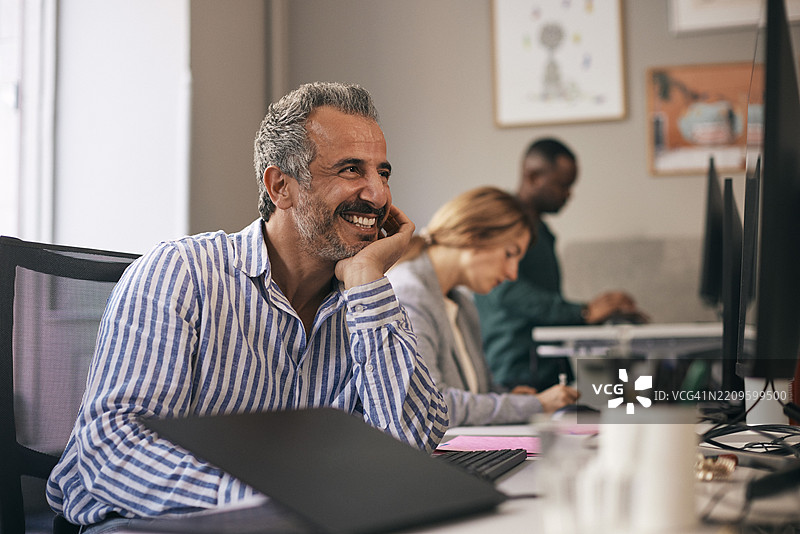 快乐的成熟创意商人在办公室的桌子上靠着肘部图片素材