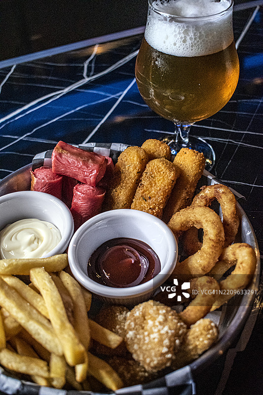 香肠、马苏里拉奶酪条、洋葱圈、裹粉鸡肉和配料薯条，以及一杯手工啤酒图片素材