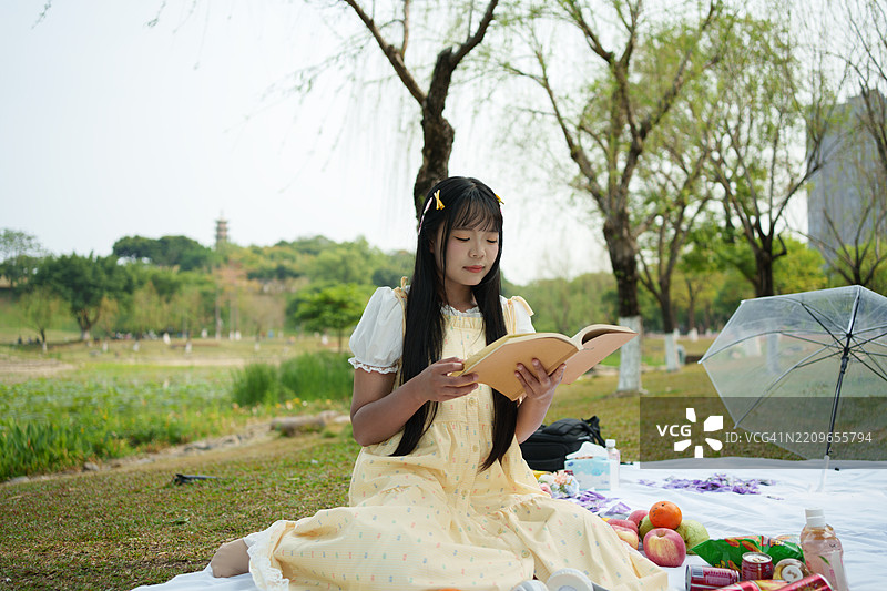 年轻的亚洲男子坐在公园里阅读一本书图片素材