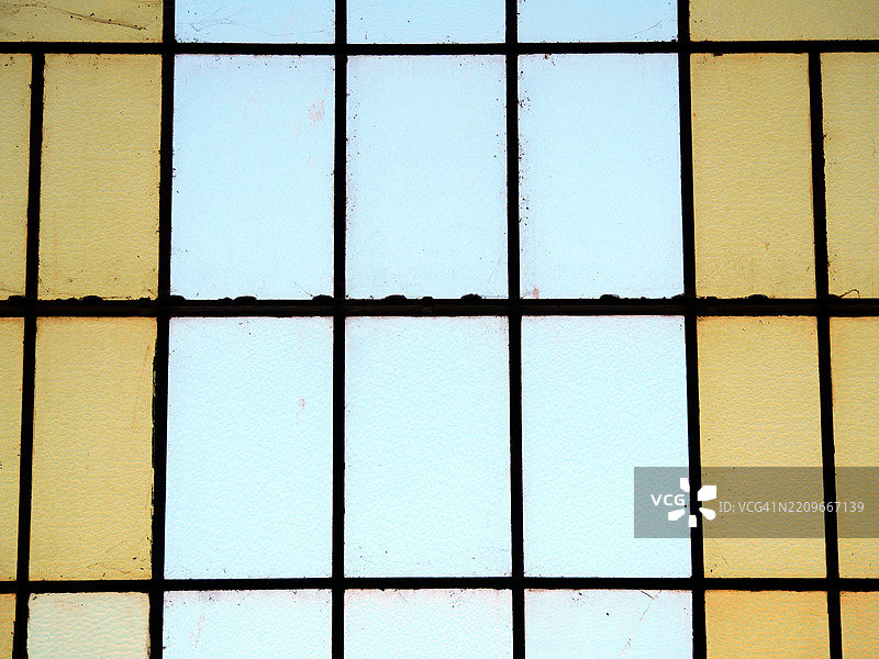 一扇风化且肮脏的窗户特写，窗户上有蓝色和黄色的矩形。葡萄牙，波尔图。阳光。图片素材