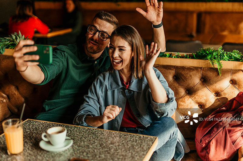 情侣在咖啡馆视频通话，向屏幕挥手。图片素材