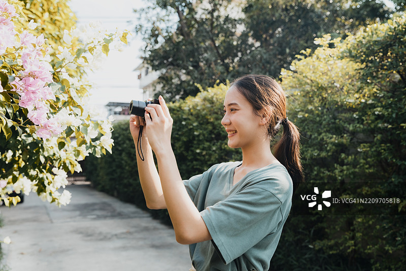 年轻女性在阳光明媚的花园里愉快地用相机拍摄花朵图片素材