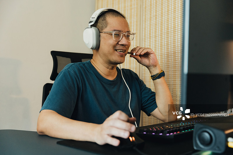 中年男子在家中使用电脑玩在线游戏。图片素材
