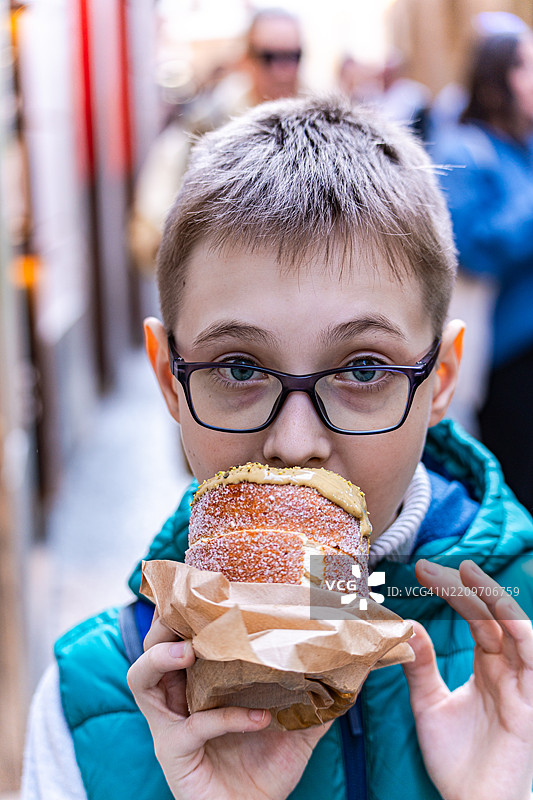 一个戴眼镜的男孩在街上吃传统的特尔德尔尼克（trdlo），布拉格，捷克共和国。图片素材