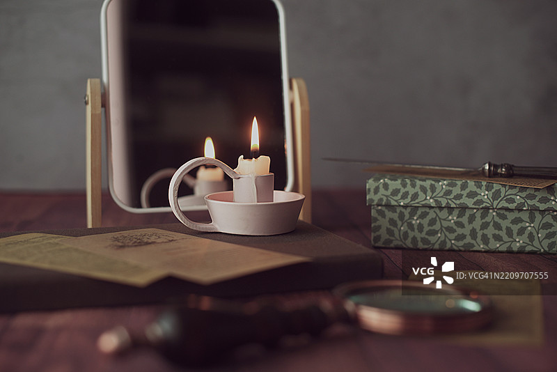 桌子上有一支点燃的蜡烛，前面是镜子，旁边有一个盒子、信件刀和放大镜。图片素材
