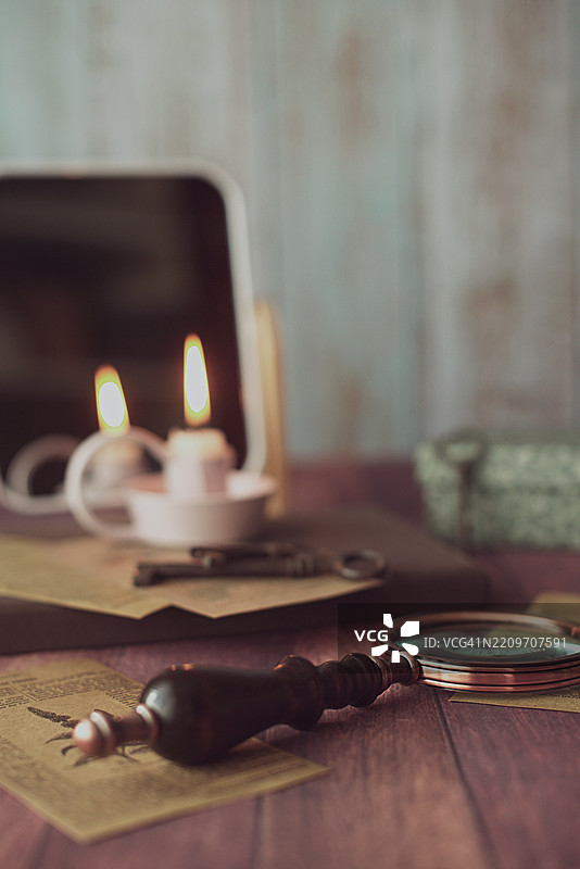 桌子上摆放着一个点燃的蜡烛，前面是镜子，旁边有一个盒子、信件刀和放大镜的特写。图片素材
