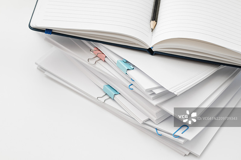 白色桌子上放着一堆文件和纸张，旁边有一台笔记本电脑图片素材