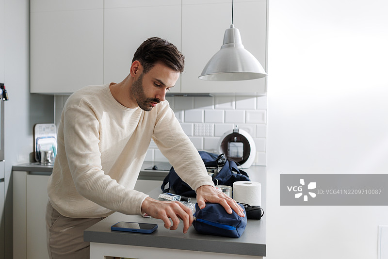 年轻男子在现代厨房里将物品整理进应急包图片素材