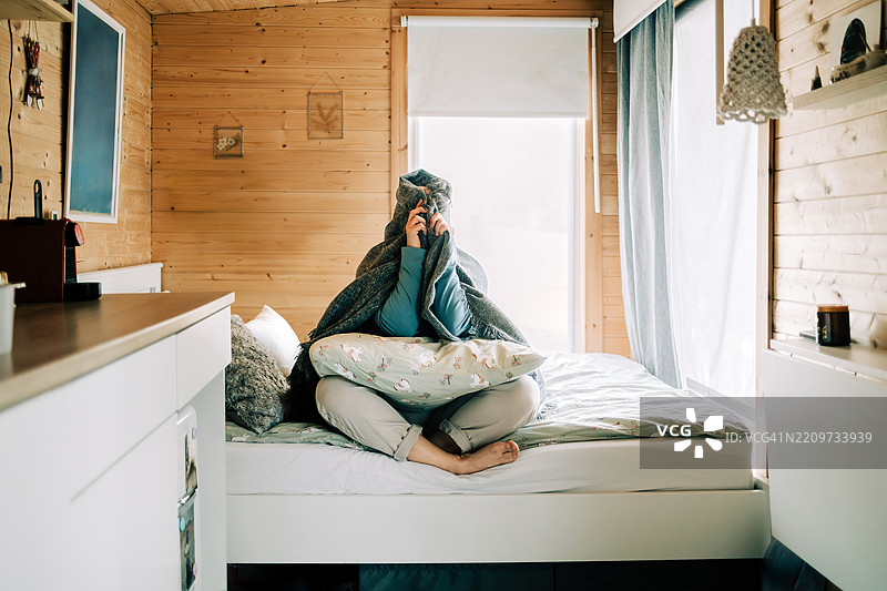 女人坐在床上，脸埋在毯子下，感到压力和焦虑。图片素材