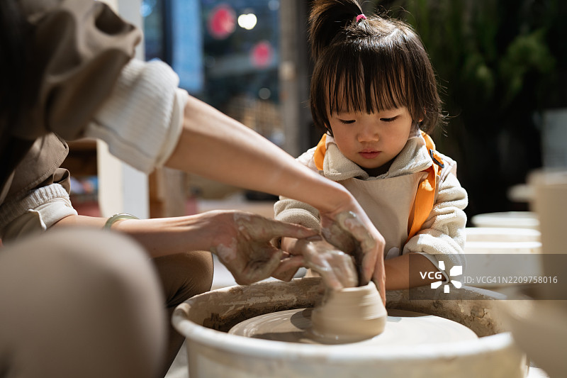 在成年人的指导下，一个孩子正在学习陶艺。图片素材