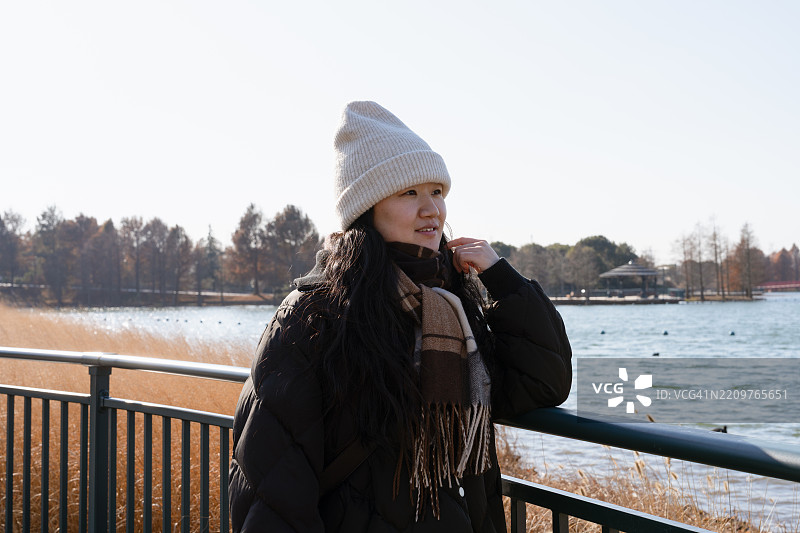 女人在湖边享受冬季风光。图片素材