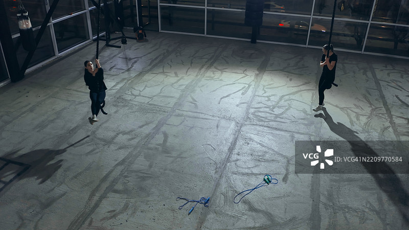 两位年轻女性在夜间的健身房里用绳子锻炼图片素材