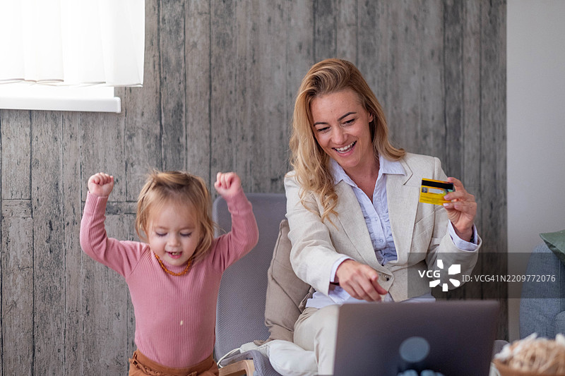 商务女性和她的女儿在公寓里看着笔记本电脑，在线购物，购物车，快乐，网购，小女孩图片素材