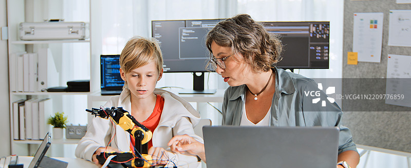 白人母亲和儿子在家用电脑和机器人手臂控制器进行家庭教育。与父母一起的年轻孩子在家学习科技知识，儿童成长概念。图片素材