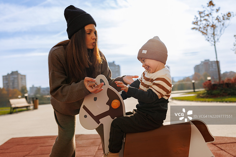 女人在公园游乐场与孩子一起骑春马，享受怀孕的快乐图片素材