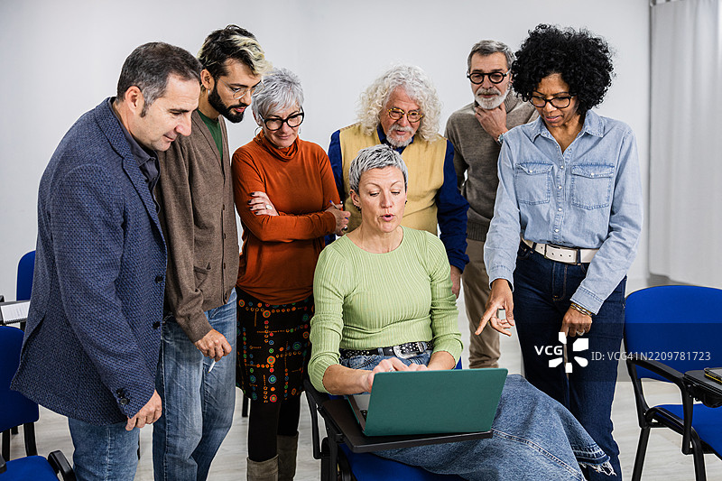 一群多元化的成年学生在教室里围绕笔记本电脑合作。图片素材