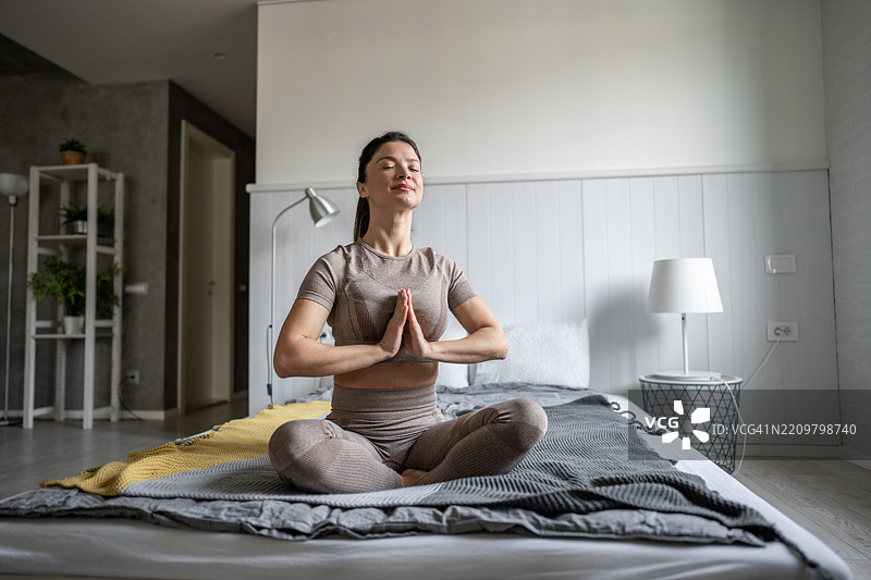 年轻女性在床上以莲花坐姿冥想图片素材