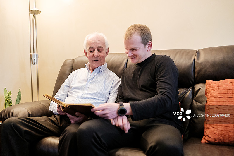 年长的父亲和成年儿子一起翻看相册，分享回忆图片素材