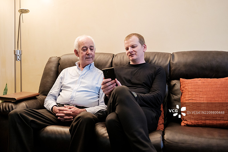 成年儿子在家里向年长父亲展示手机上的内容图片素材
