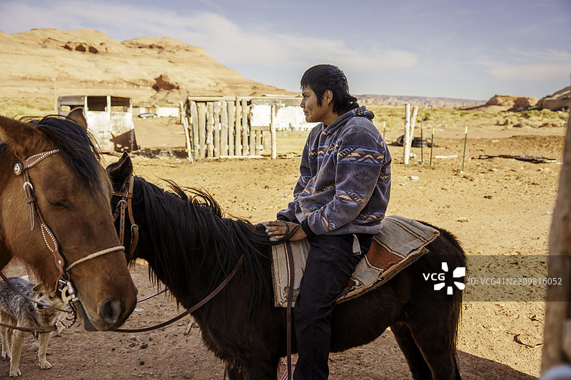 十五岁的纳瓦霍少年坐在马背上，准备在美国西南部的沙漠牧场骑行，靠近犹他州/亚利桑那州的纪念碑谷部落公园。图片素材