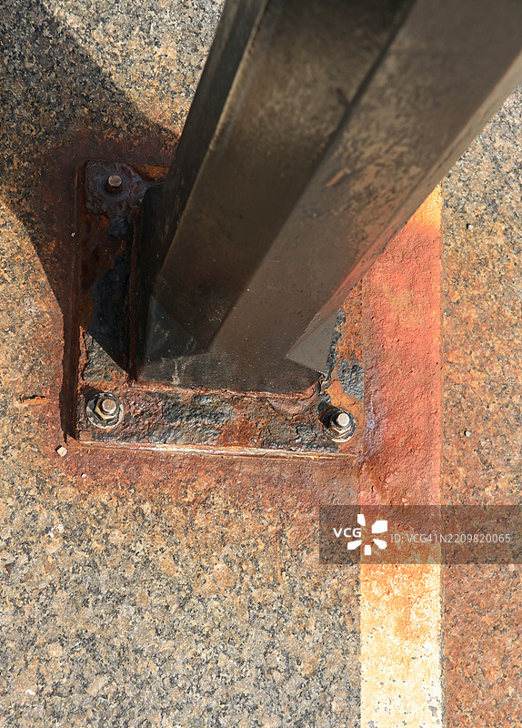 生锈的金属柱子固定在石质人行道上，是楼梯栏杆的一部分图片素材