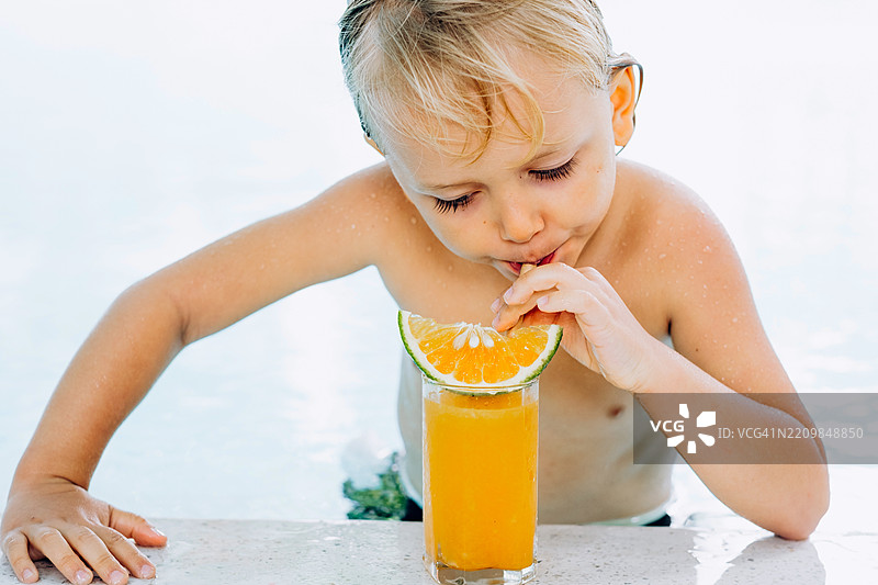 小男孩在游泳池旁喝橙汁。图片素材