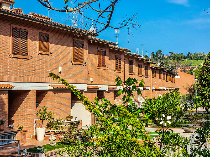 现代郊区住宅，砖砌外墙，木制百叶窗，天线和繁茂的花园，映衬在宁静的蓝天之下，营造出宁静的生活氛围。图片素材