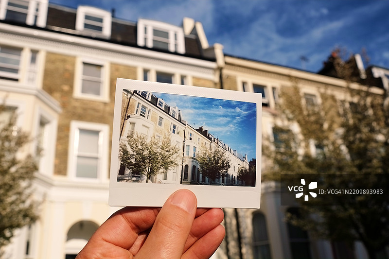男子在伦敦一排联排别墅前手持即时胶卷照片图片素材