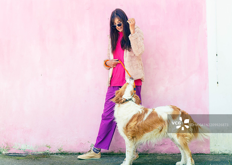 女人在粉色墙壁旁与她的狗玩耍图片素材