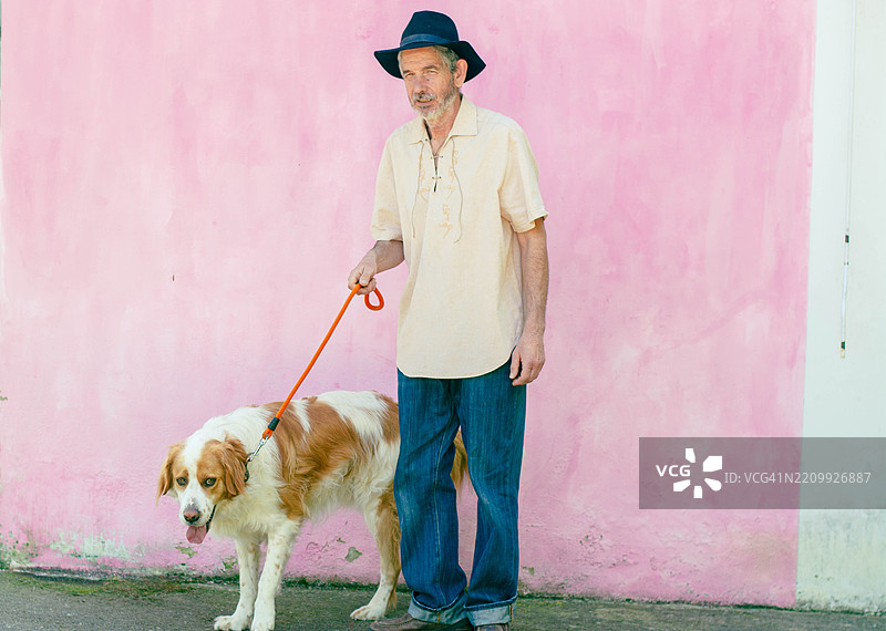 一位老年男子在粉色墙壁前牵着狗散步图片素材