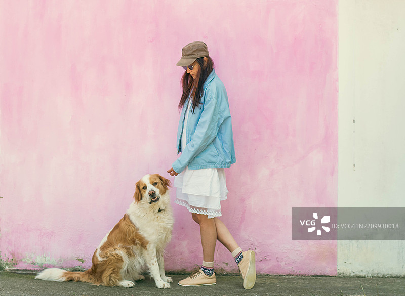 年轻女性在粉色墙前遛狗图片素材
