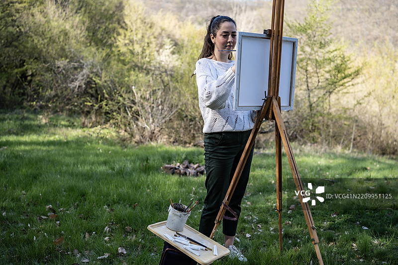 年轻女性在宁静的户外环境中用画架作画图片素材