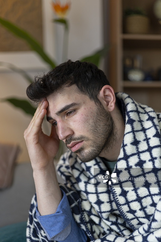 生病的年轻人裹着毯子在家中忍受头痛图片素材