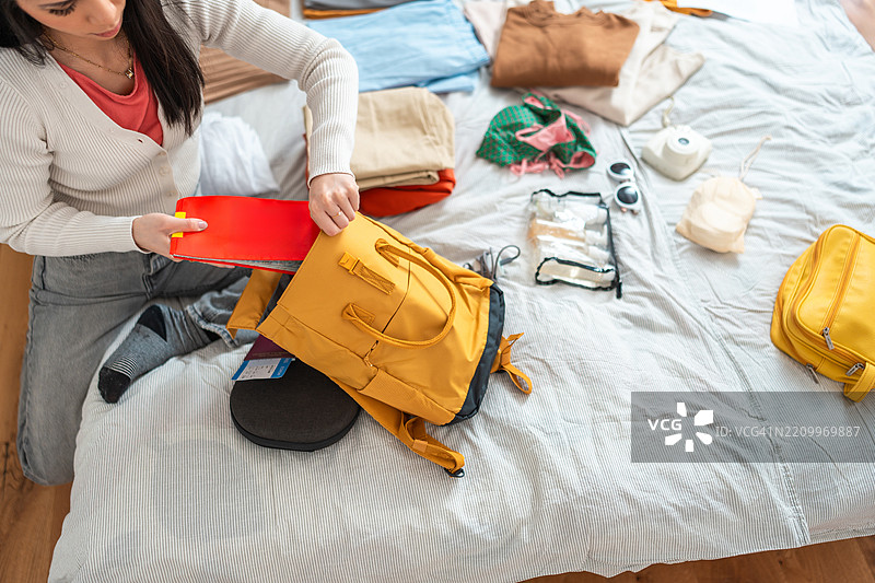 年轻亚洲女性在白色床上整理装有旅行必需品的黄色背包图片素材