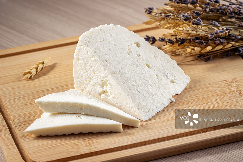 切片白色奶酪放在竹板上。干小麦和薰衣草枝条营造出乡村风格的摆盘。图片素材