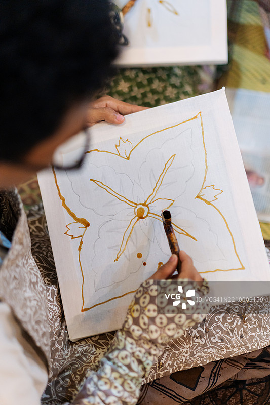 年轻男子在工作坊中近距离视角涂抹蜡于蜡染花卉图案上图片素材