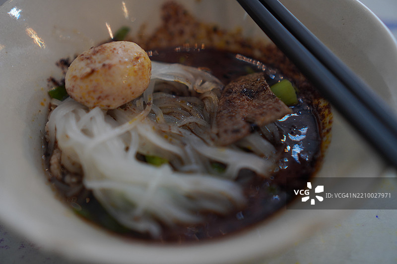 泰式面条，白碗中盛着小面条、炖猪肉、肉丸、猪肝和血汤，搭配木筷和勺子，调味后美味的泰国菜。图片素材