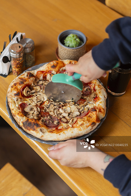 穿着白色制服的厨师在切披萨的特写手部。图片素材