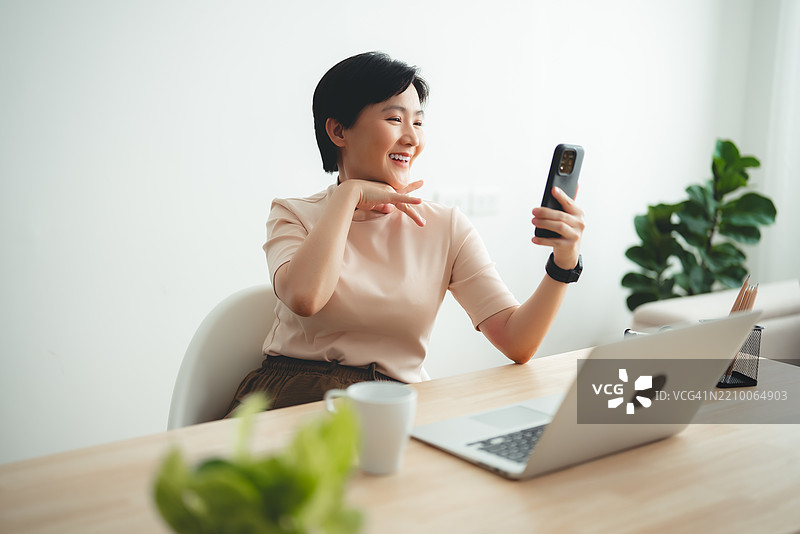 亚洲女性在家办公时享受使用智能手机进行视频会议或自拍。图片素材