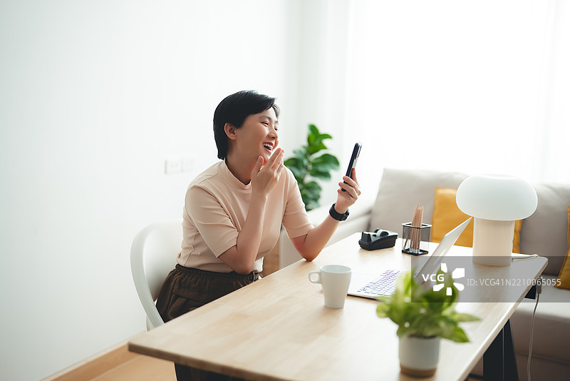 亚洲女性在家办公时享受使用智能手机进行视频会议或自拍。图片素材