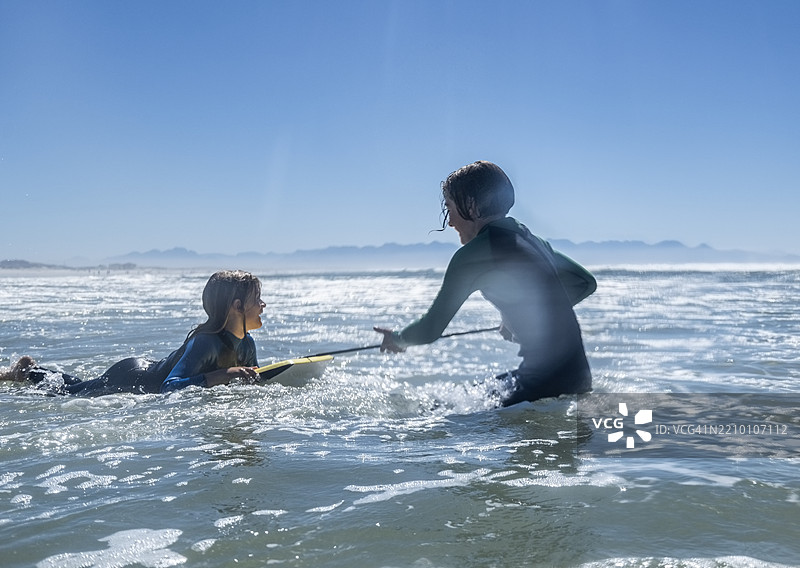 青少年在海洋中拉着弟弟玩冲浪板图片素材