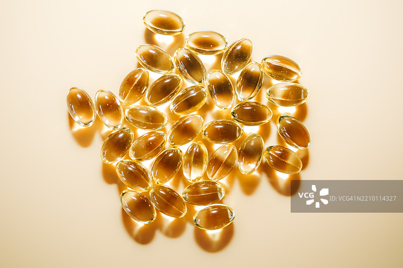 透明黄色油状物质的软胶囊在米色背景下反射阳光图片素材