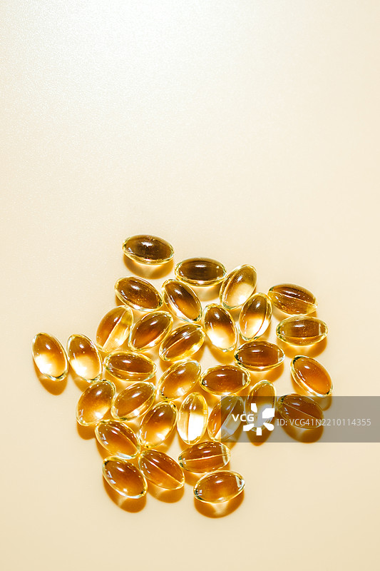 透明黄色油状物质的软胶囊在米色背景上反射阳光图片素材